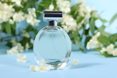 Aromatic perfume in bottle and beautiful jasmine flowers on light blue background, closeup