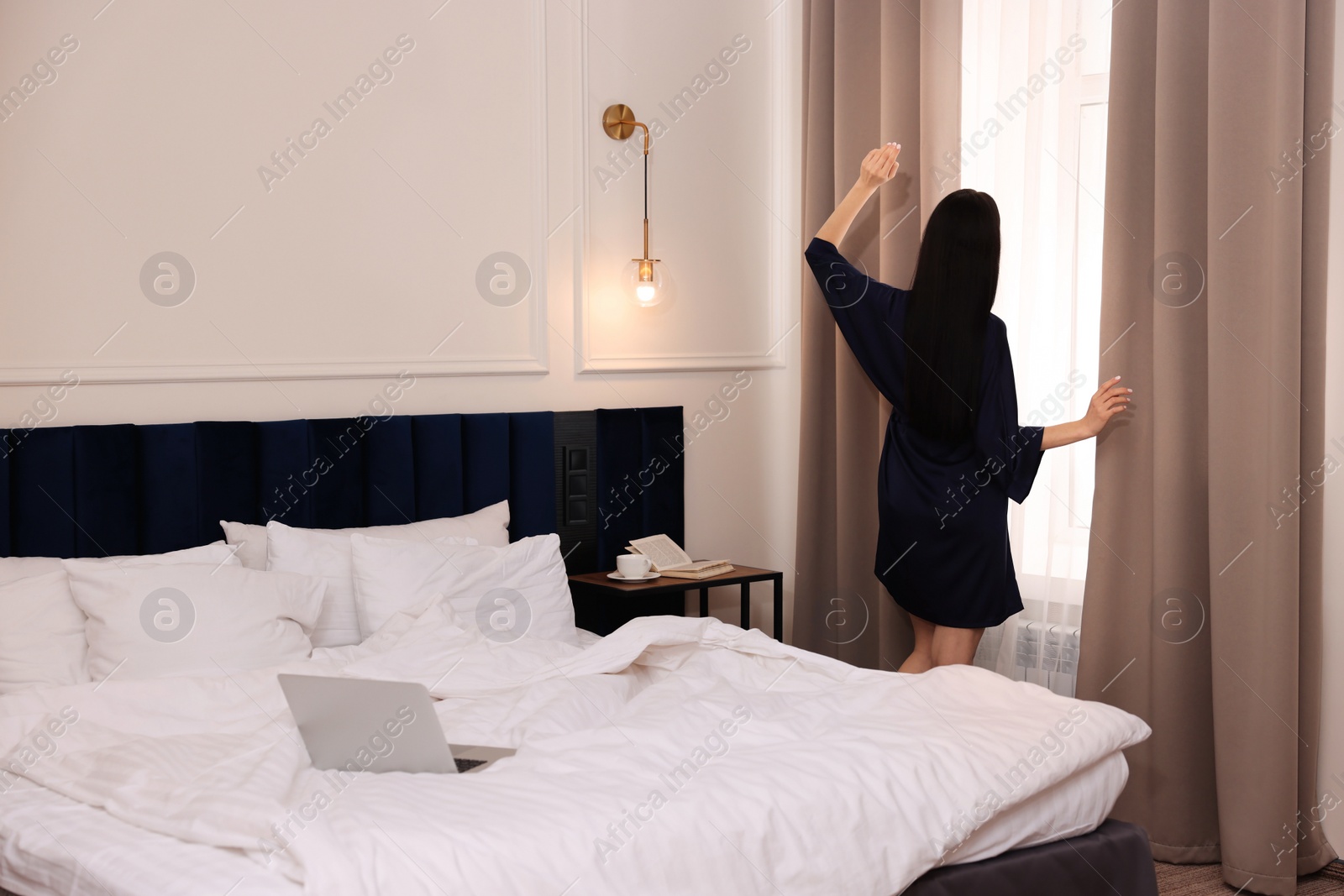 Photo of Beautiful young woman wearing silk robe near window in hotel room