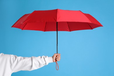 Photo of Woman with open red umbrella on light blue background, closeup
