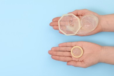 Photo of Woman with unrolled female and male condoms on light blue background, top view. Space for text