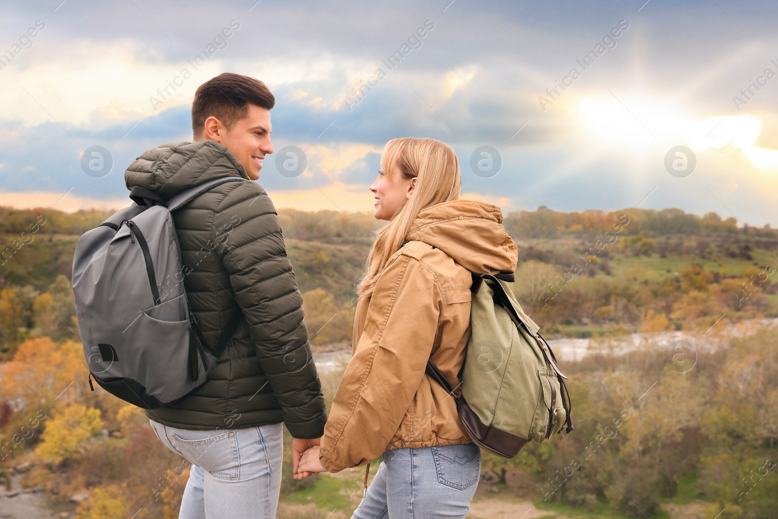 Photo of Couple of hikers with travel backpacks enjoying beautiful view near mountain river