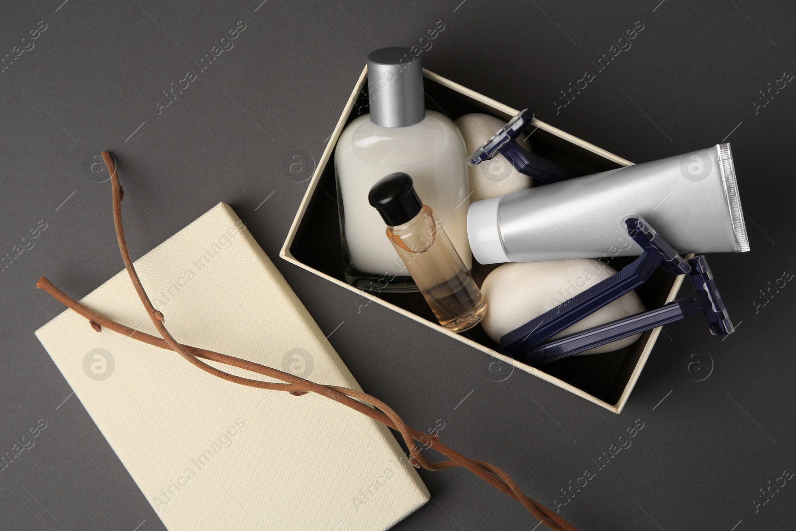 Photo of Box, different men's shaving accessories and dry branches on dark grey background, flat lay