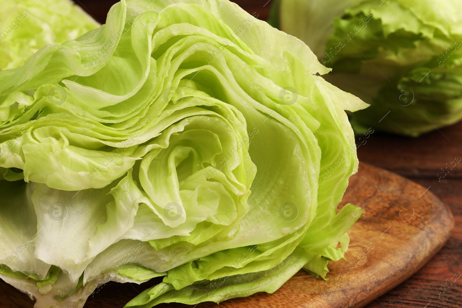 Photo of Board with half of fresh green iceberg lettuce head on wooden table, closeup