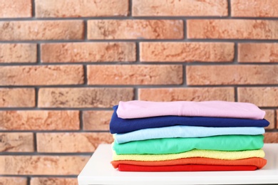 Photo of Stack of rainbow clothes on table against brick wall background