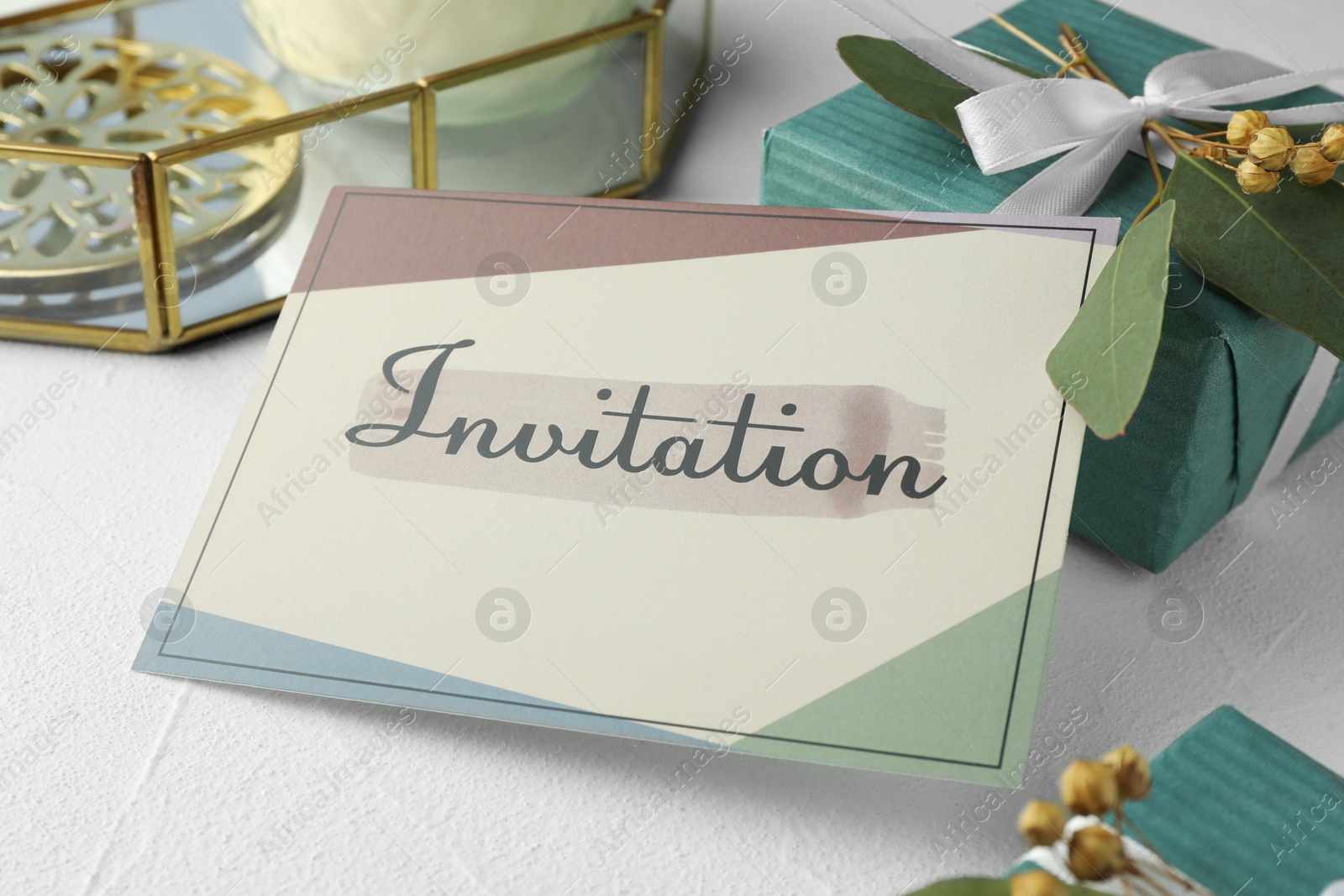 Photo of Beautiful card with word Invitation, eucalyptus leaves and gift boxes on white table, closeup