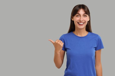 Special promotion. Happy woman pointing at something on light grey background, space for text