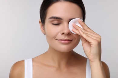 Photo of Young woman cleaning her face with cotton pad on light grey background