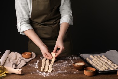 Woman making homemade breadsticks at wooden table indoors, closeup. Cooking traditional grissini