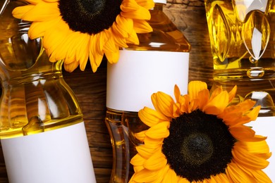Photo of Bottles of sunflower cooking oil and beautiful flowers on wooden table, top view