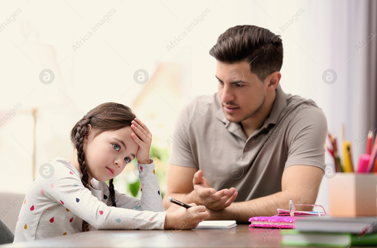 Photo of Father scolding his daughter while helping with homework at table indoors