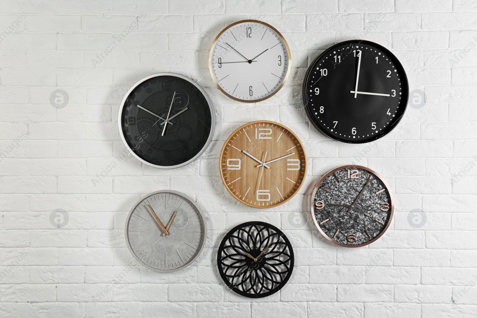 Photo of Different analog clocks hanging on white wall. Time of day