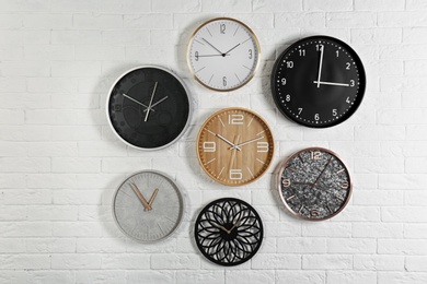 Photo of Different analog clocks hanging on white wall. Time of day