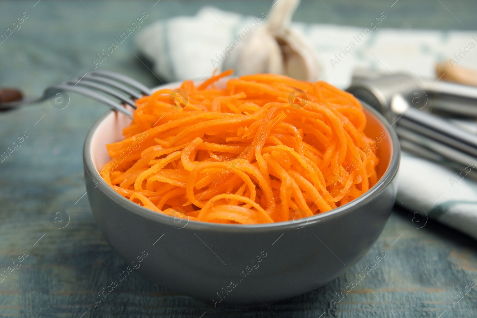 Photo of Delicious Korean carrot salad in bowl on blue wooden table