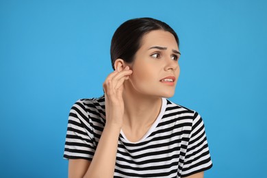 Young woman suffering from ear pain on light blue background