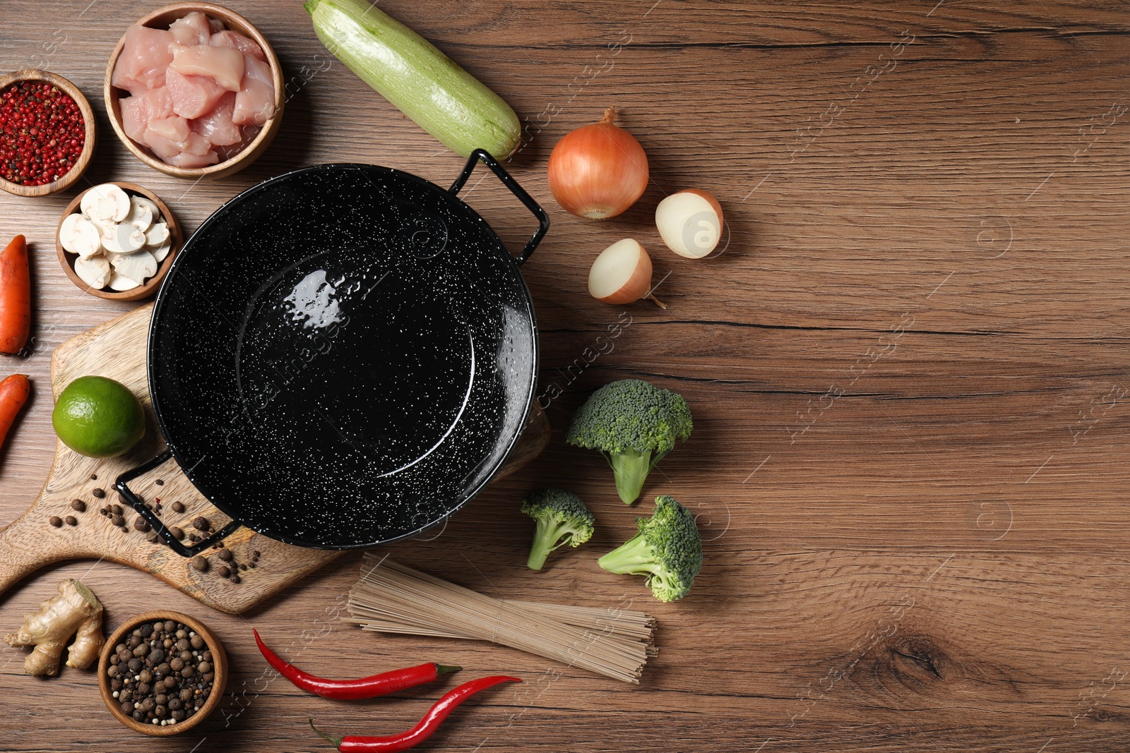 Photo of Empty iron wok surrounded by raw ingredients on wooden table, flat lay