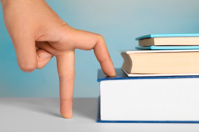 Photo of Woman imitating stepping up on books with her fingers against light blue background, closeup
