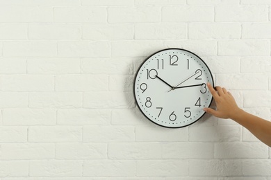 Photo of Woman touching clock on white brick wall, space for text. Time management