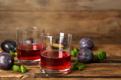 Photo of Delicious plum liquor, mint and ripe fruits on wooden table. Homemade strong alcoholic beverage
