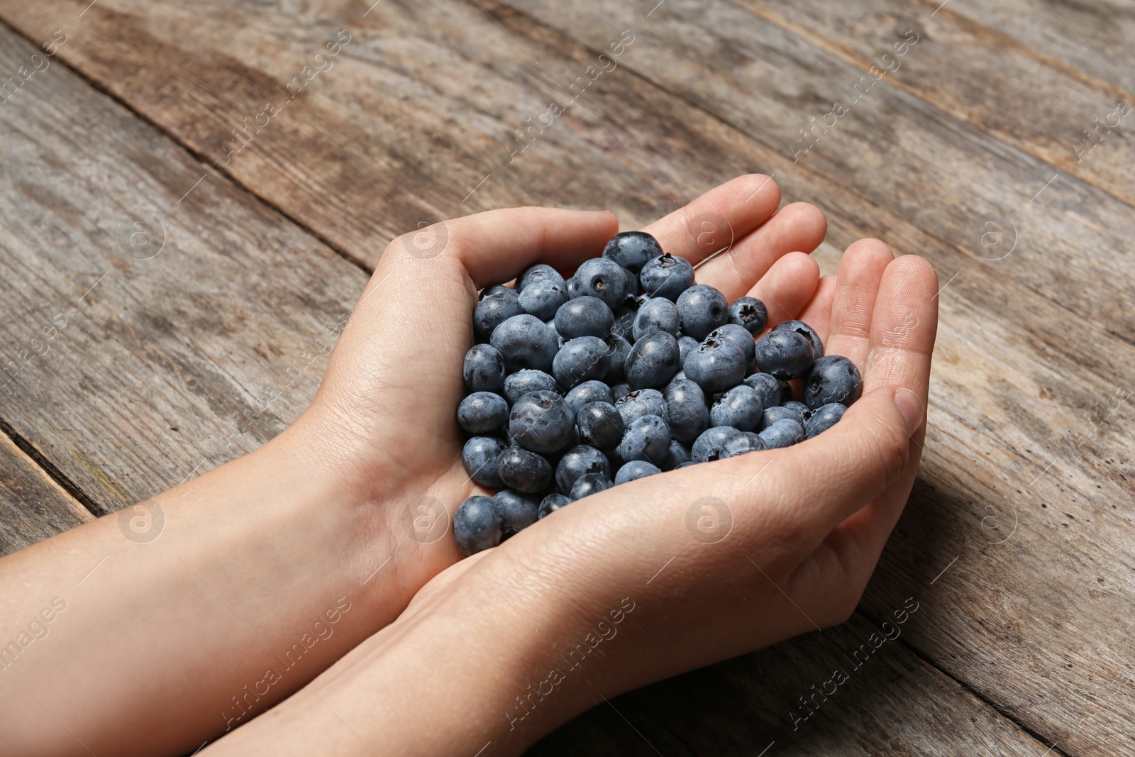 Photo of Woman holding juicy fresh blueberries on wooden table