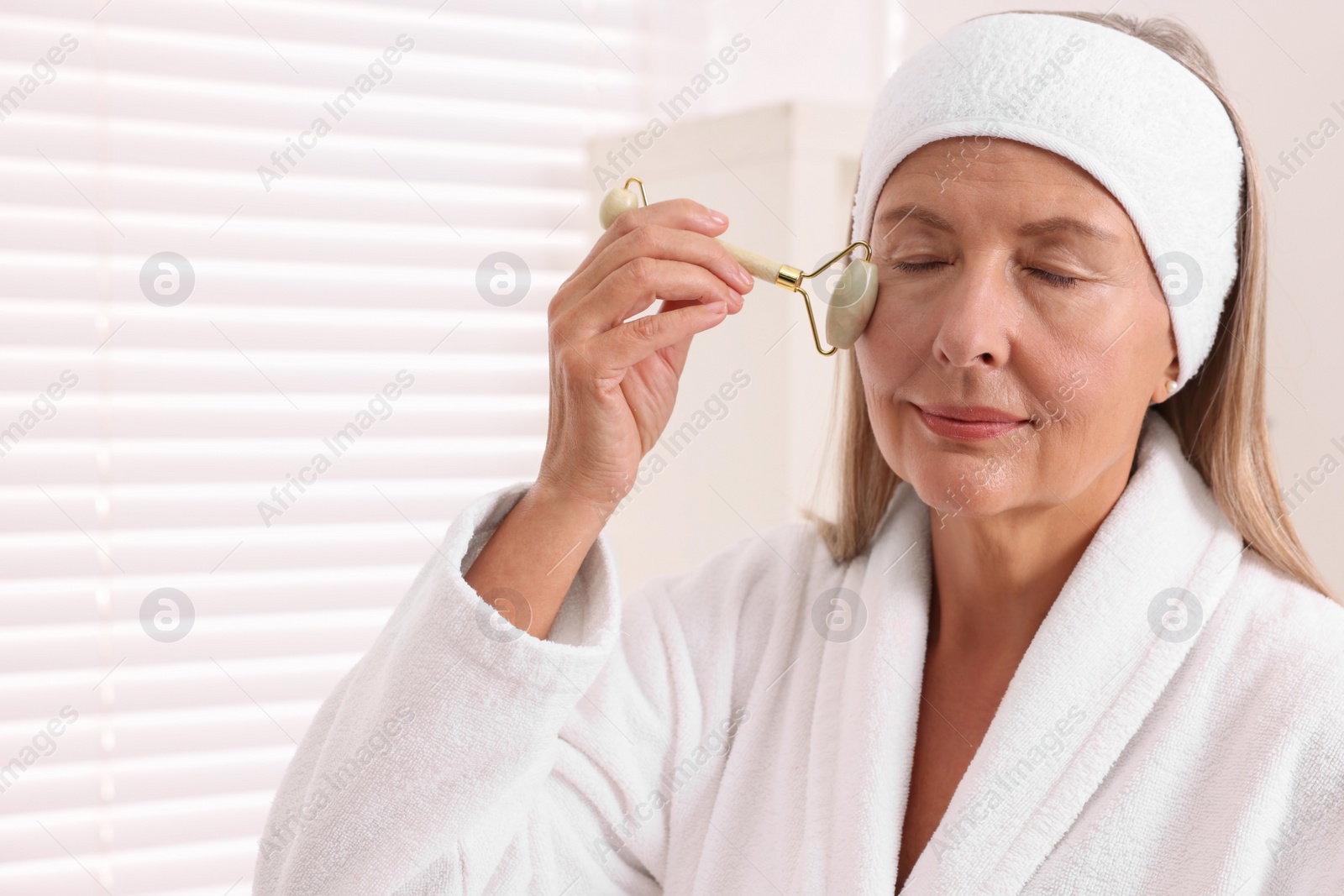 Photo of Woman massaging her face with jade roller in bathroom. Space for text