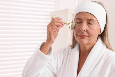 Photo of Woman massaging her face with jade roller in bathroom. Space for text