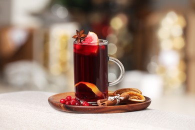 Aromatic mulled wine in cup and ingredients on sofa armrest against blurred background