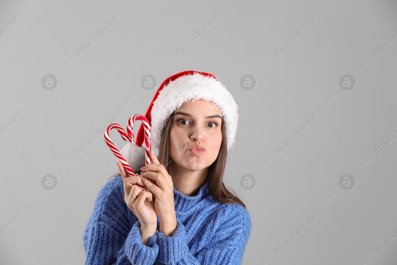 Photo of Pretty woman in Santa hat and sweater making heart with candy canes on grey background
