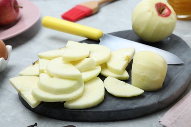 Photo of Cut fresh apple with knife and board on grey table, closeup. Baking pie
