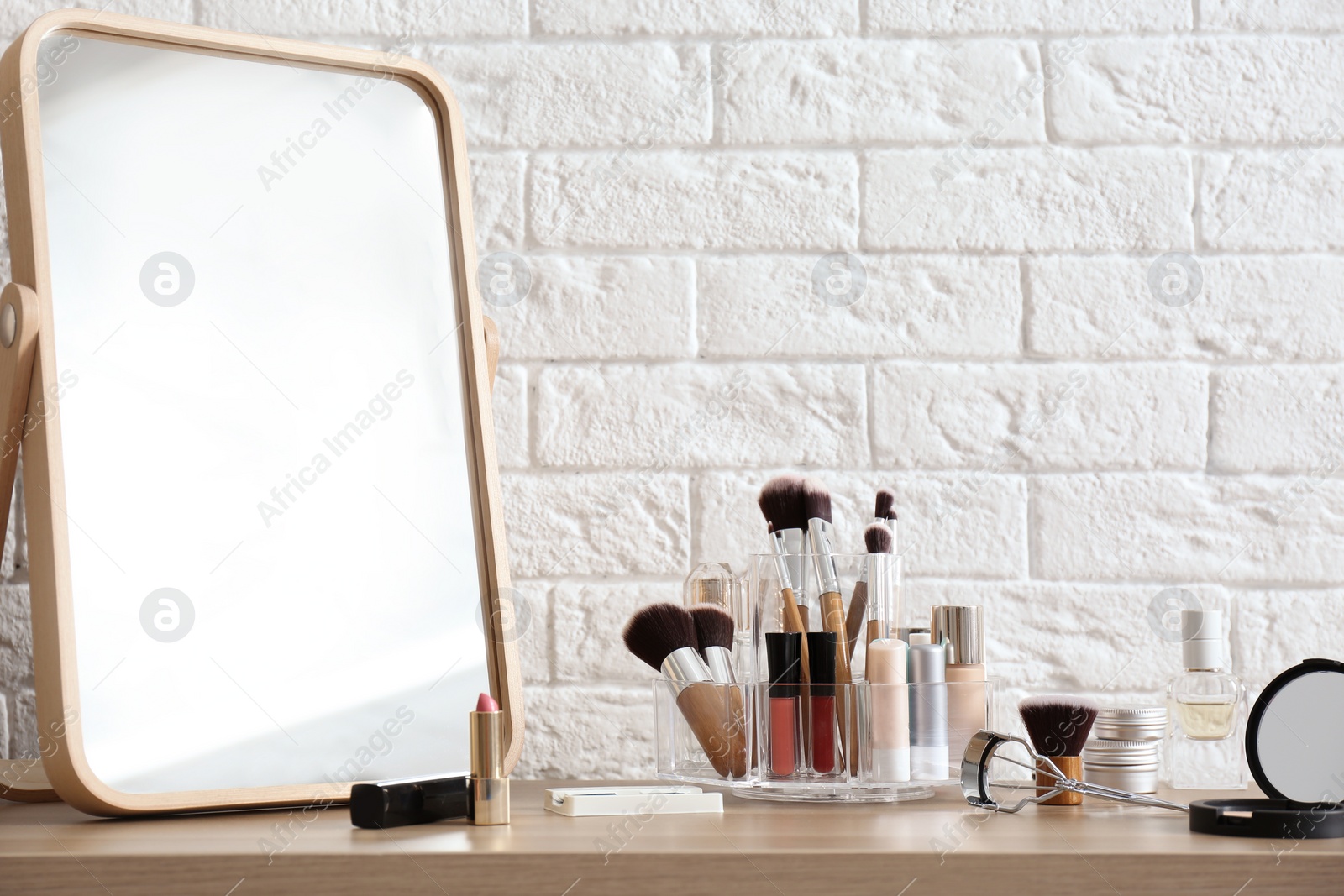 Photo of Organizer with cosmetic products for makeup on table near brick wall