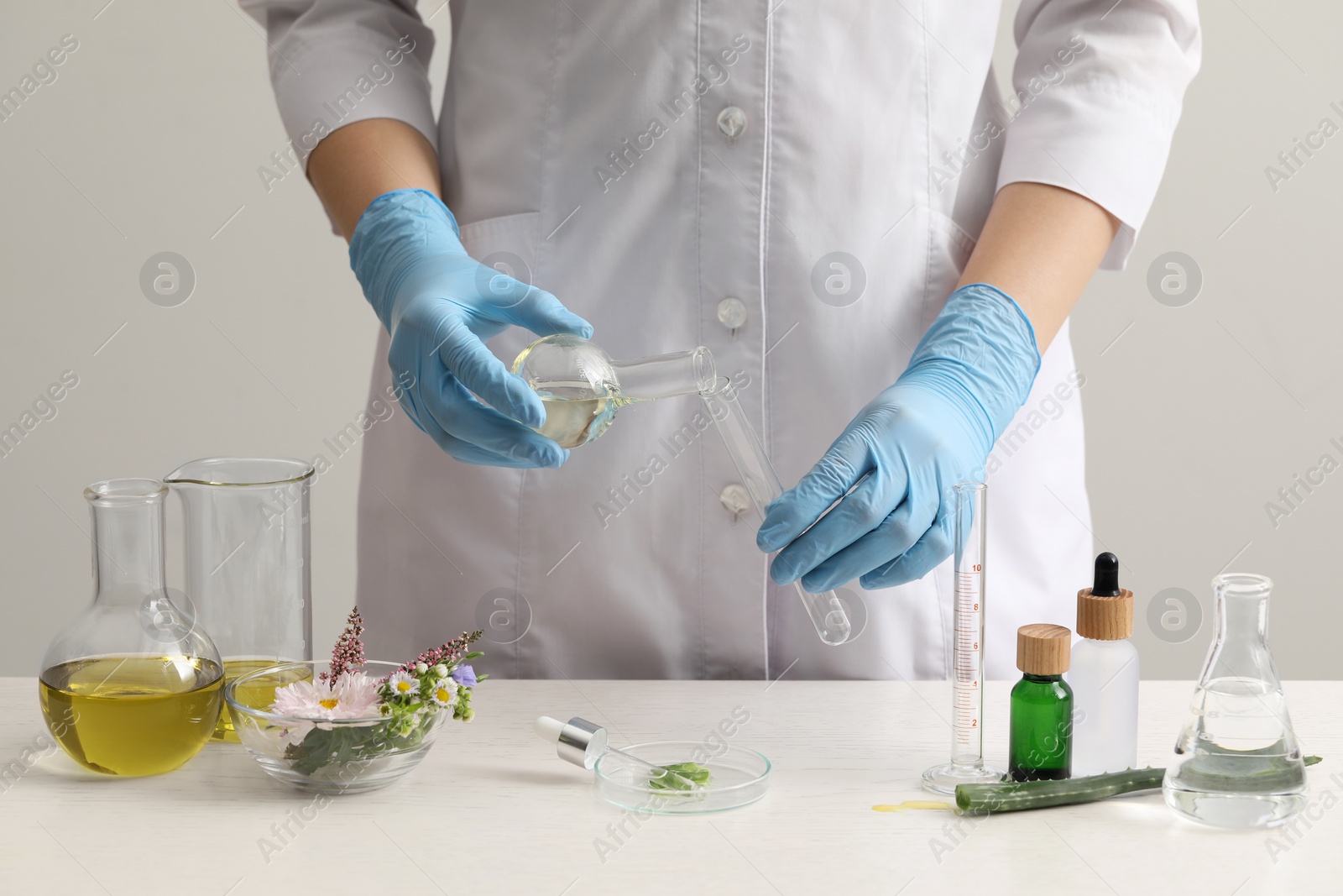 Photo of Scientist developing cosmetic oil at white table, closeup