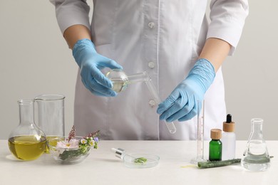 Scientist developing cosmetic oil at white table, closeup