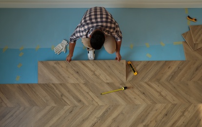 Photo of Professional worker installing new parquet flooring indoors, top view