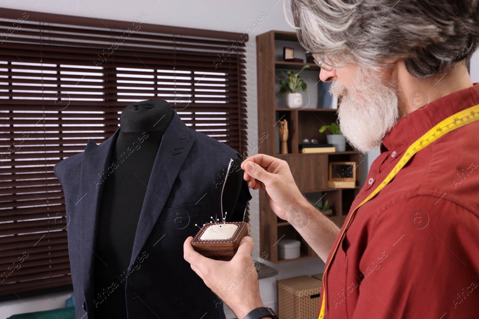 Photo of Professional tailor with pin cushion working in atelier