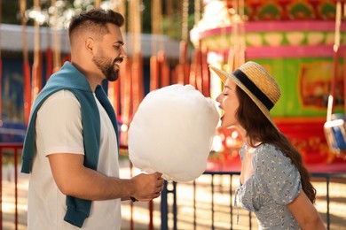Happy young man and his girlfriend eating cotton candy at funfair