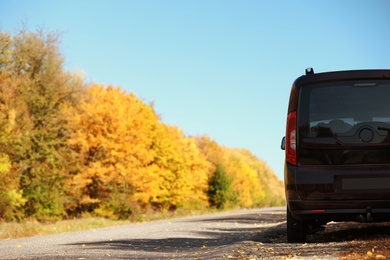 Photo of Car parked on country road near autumn forest. Space for text