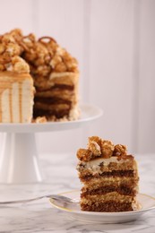 Photo of Piece of caramel drip cake decorated with popcorn and pretzels on white marble table