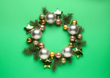 Beautiful festive wreath made of different Christmas balls and fir tree branches on green background, top view