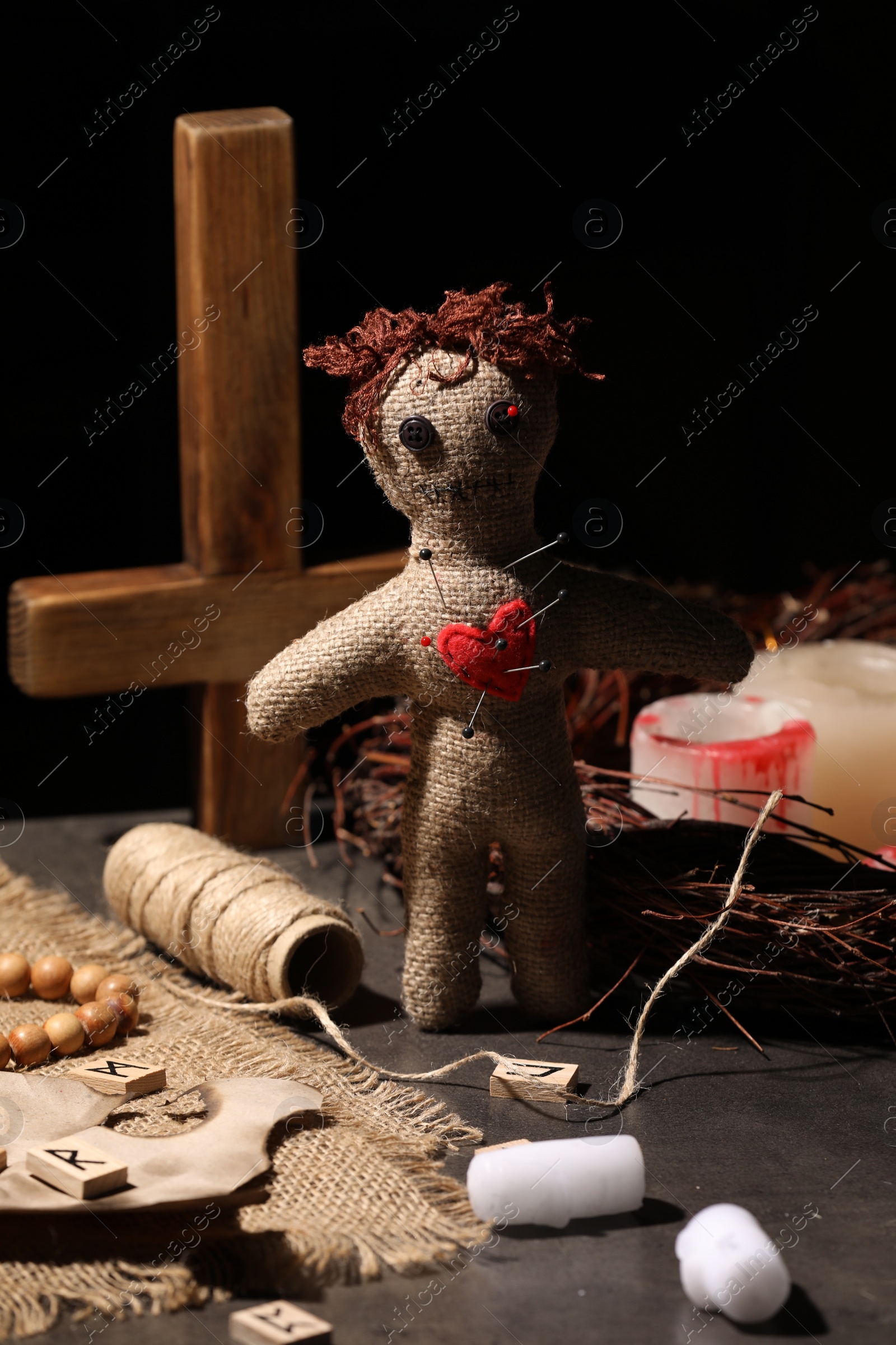 Photo of Voodoo doll with pins in heart and ceremonial items on black table