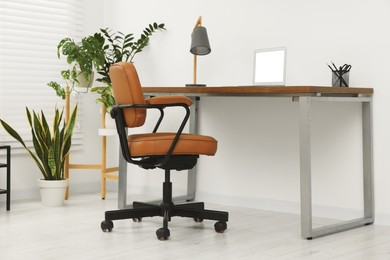 Photo of Stylish office interior with comfortable chair, desk, laptop and houseplants