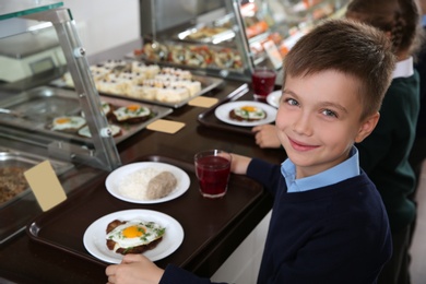 Photo of Cute boy near serving line with healthy food in school canteen