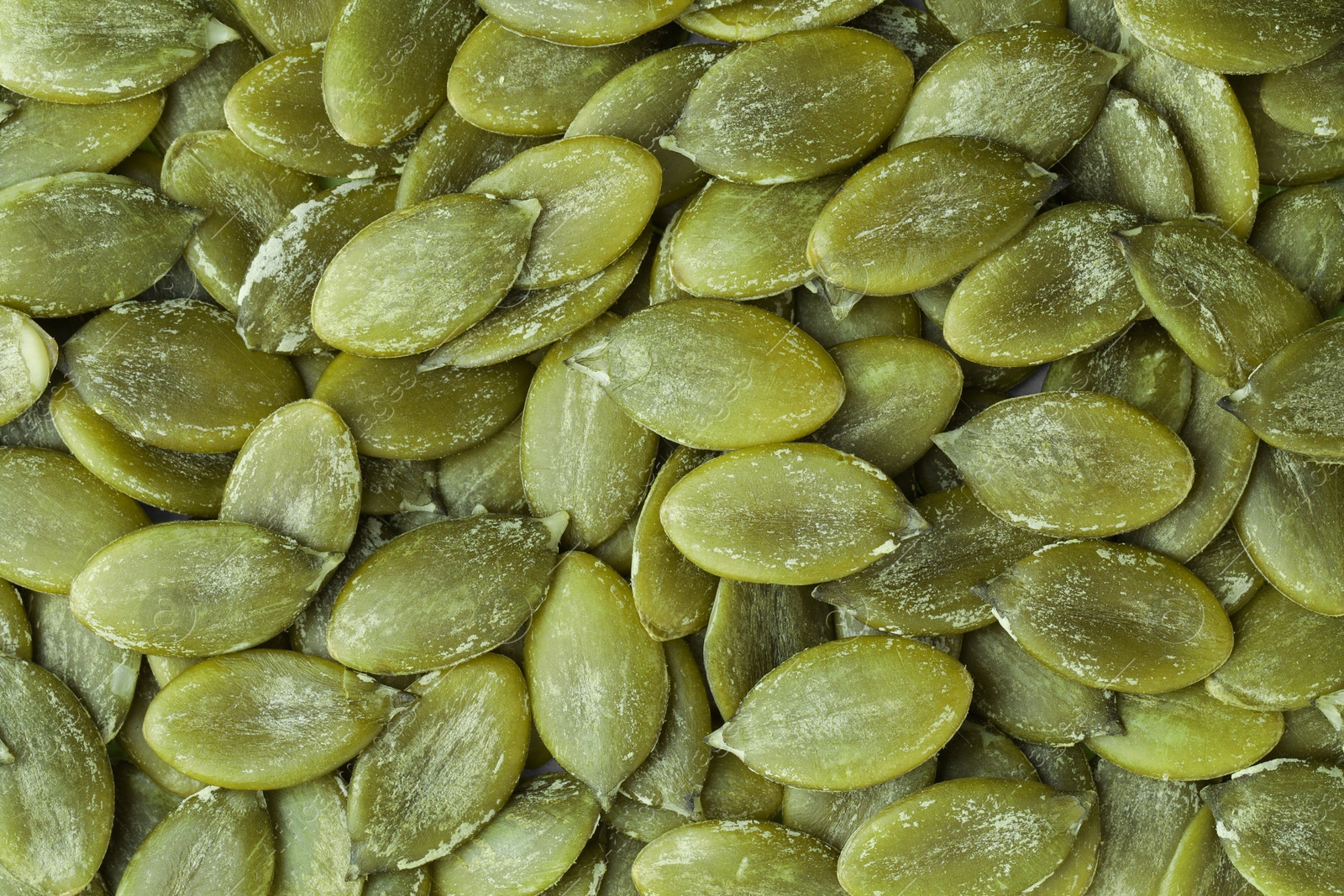 Photo of Many peeled pumpkin seeds as background, top view