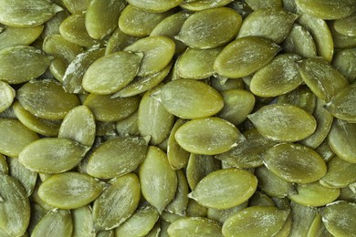 Photo of Many peeled pumpkin seeds as background, top view