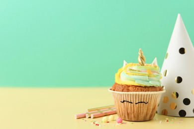 Photo of Cute sweet unicorn cupcake and party items on yellow table, space for text