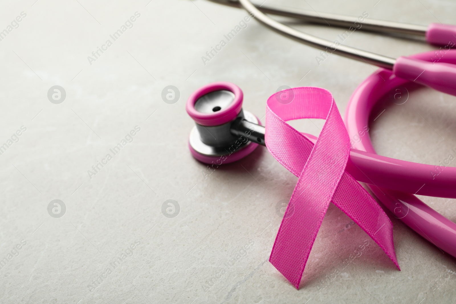 Photo of Pink ribbon and stethoscope on grey background, space for text. Breast cancer concept