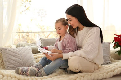 Photo of Mother and daughter making paper snowflake near window at home