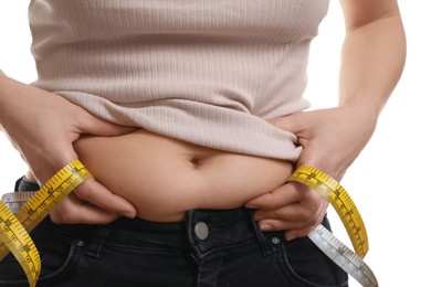 Woman with measuring tape touching belly fat on white background, closeup. Overweight problem