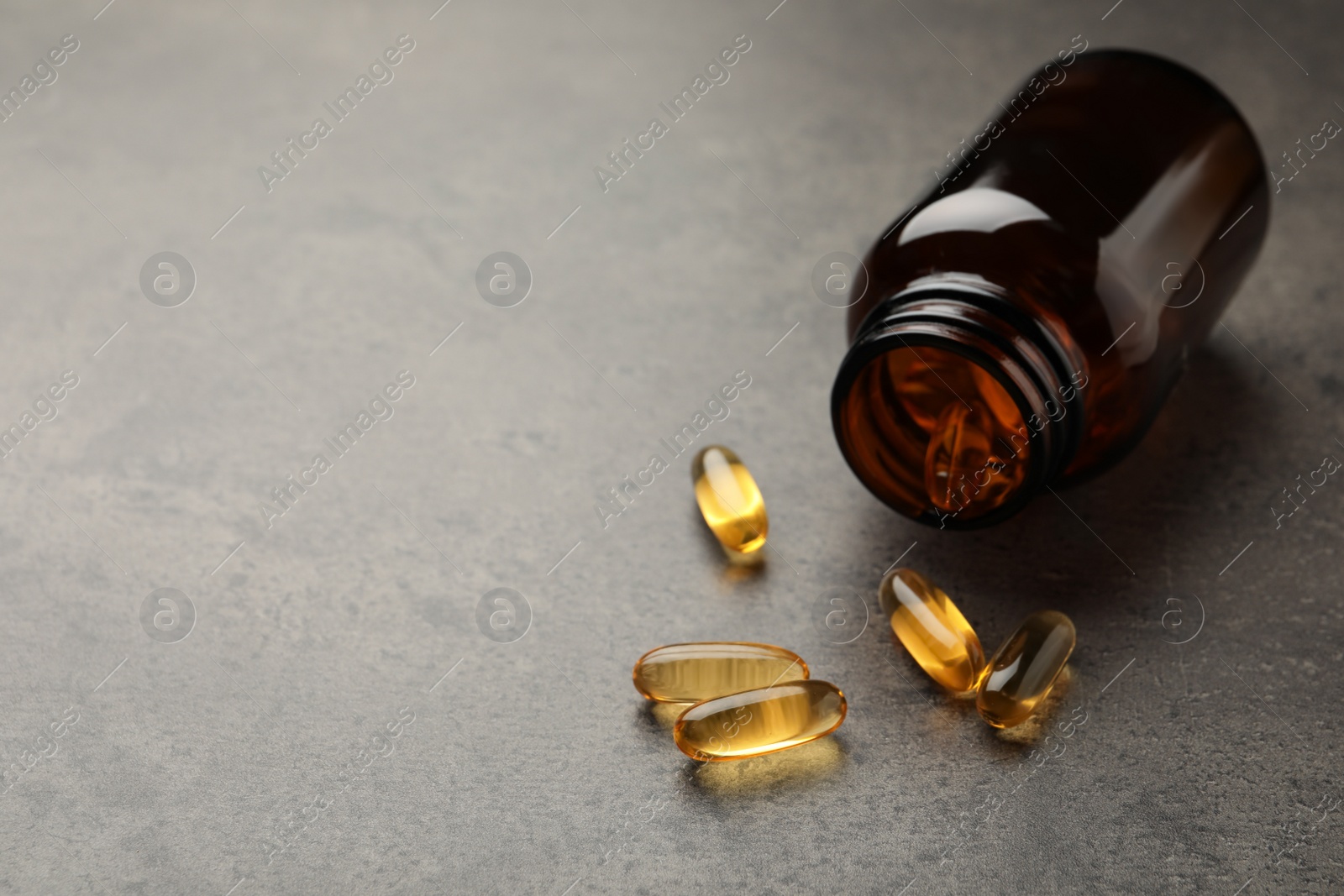 Photo of Overturned bottle with dietary supplement capsules on grey table. Space for text