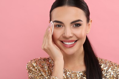 Photo of Beautiful woman removing makeup with cotton pad on pink background. Space for text