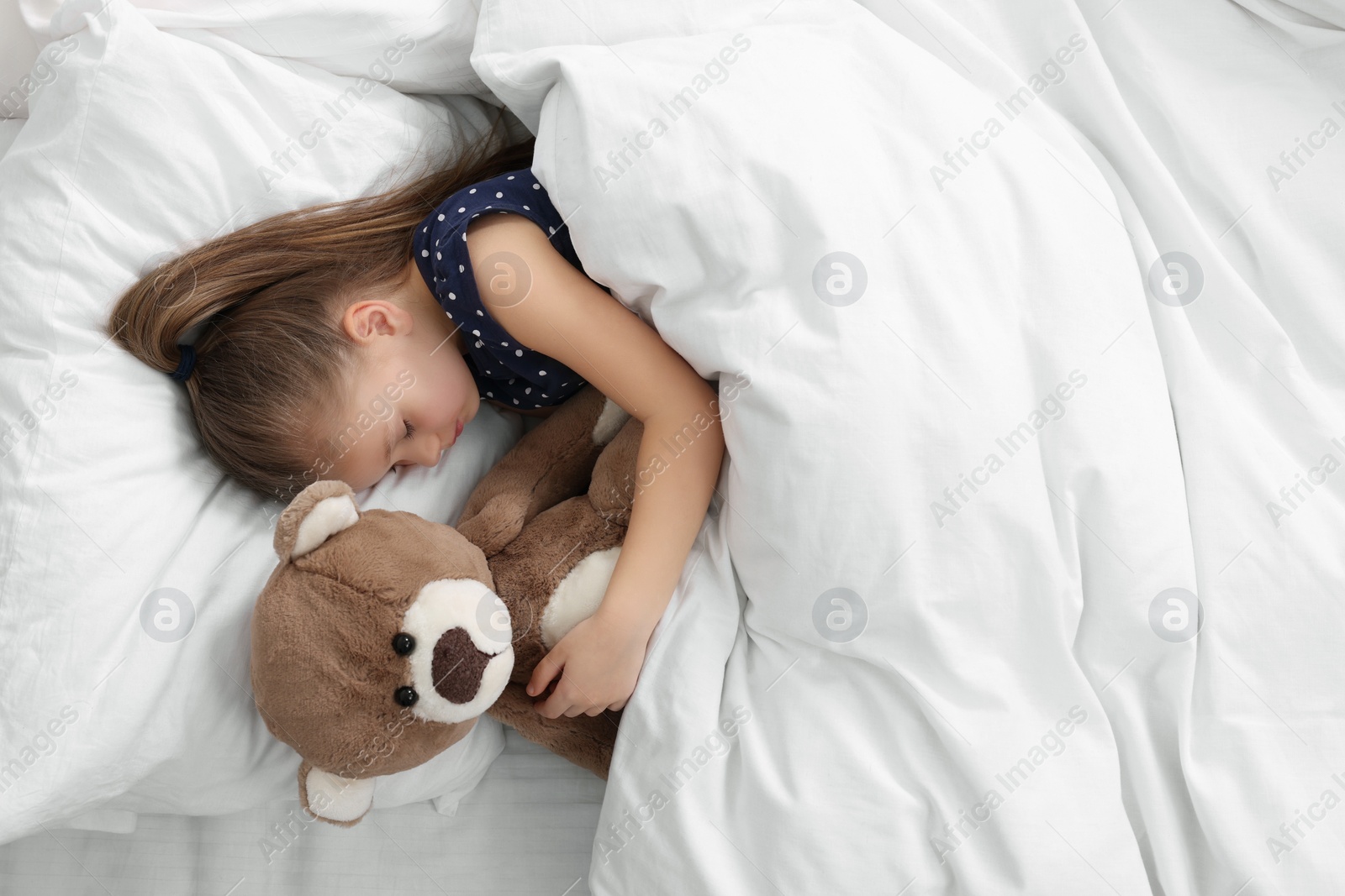 Photo of Cute little girl sleeping with teddy bear in bed, top view. Space for text