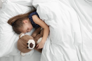 Cute little girl sleeping with teddy bear in bed, top view. Space for text